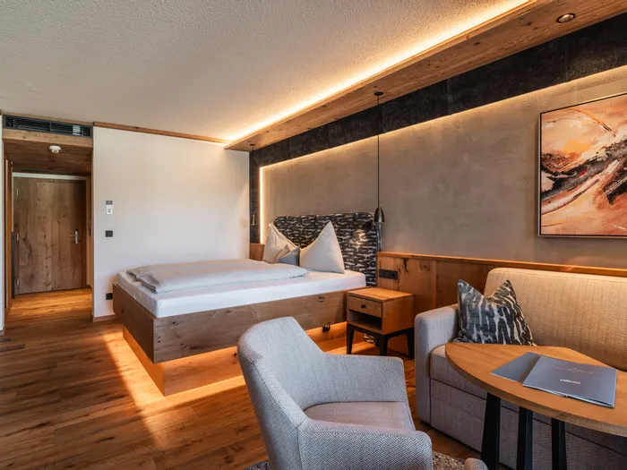 Modernes Hotelzimmer mit Holzmöbeln, gemütlichem Bett, Sofa, Sessel und stimmungsvoller Beleuchtung